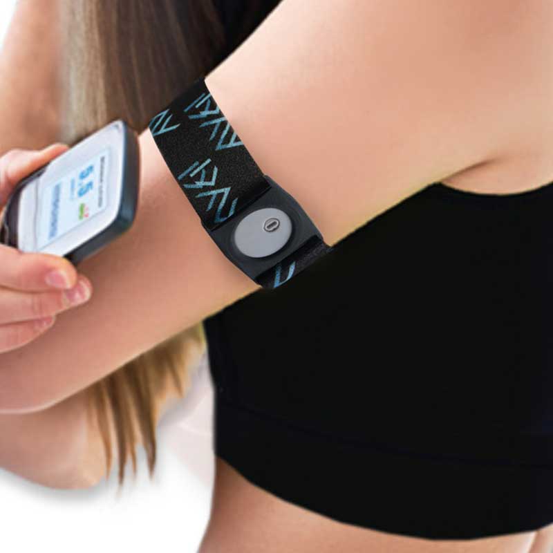 Person wearing a Freestyle Libre 3 armband on their upper arm, holding the glucose monitor to check levels. The black armband with blue patterns provides a snug fit for sports and activities. Obraz