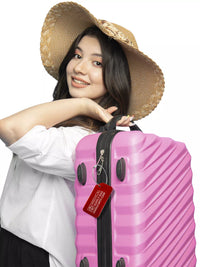Smiling woman with a hat carrying a pink suitcase with a red 'Medical Supply Bag Handle With Care' luggage tag attached.
